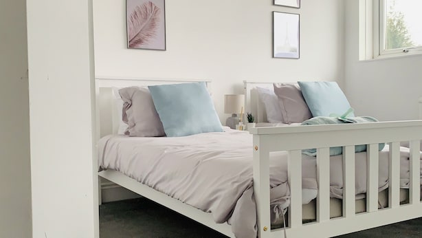 A bedroom with a white bed, light blue pillows, and framed pictures on the wall. - Impeccable 3 bed House in Brentwood (Brentwood)