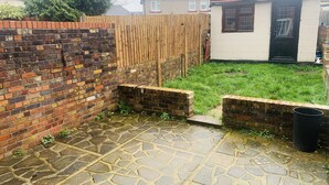 A paved patio area with a brick wall and a wooden fence. - Impeccable 3 bed House in Brentwood (Brentwood)