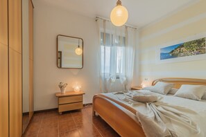 Une chambre à coucher avec un lit, des tables de chevet, un miroir, une fenêtre avec des rideaux légers et un tableau au mur.