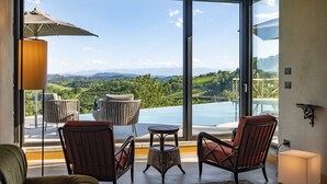 A room with large windows overlooking a pool and mountains. There are two chairs and a small table. - Relais Casa Clara (Monteu Roero)