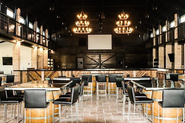 Conference room with a rustic yet modern ambiance, featuring a large presentation screen, ornate chandeliers, and comfortable seating.