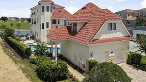 Uma casa de dois andares com telhado de telhas vermelhas, piscina e um jardim bem cuidado.