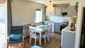 A compact kitchen with white cabinets, a dining table with chairs, a sofa, and a hanging light fixture.