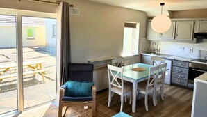 A modern kitchen with white cabinets, a dining area with a glass table and white chairs, a blue cushioned chair, and a view of the outside patio.