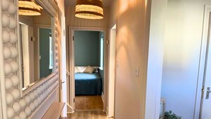 A narrow hallway with a bed in the background, a radiator on the left, and a potted plant on the right.