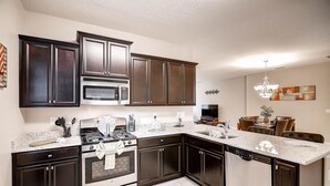 A modern kitchen with dark cabinetry, stainless steel appliances, and a granite countertop. - 4329ac - Solterra Gated Resort 5 Bedroom Home by RedAwning (Davenport)