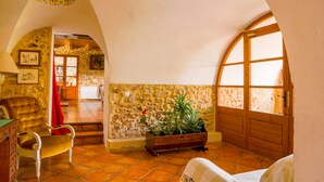 Una habitación acogedora con pared de piedra, puerta de madera, una silla roja, un banco de madera con plantas y una cama.