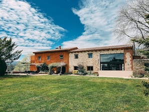 Una casa de dos pisos con fachada de piedra, ventanas amplias y un césped cuidado.