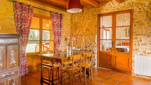 Una cocina rústica con pared de piedra, mesa de madera, sillas y una lámpara roja colgante.
