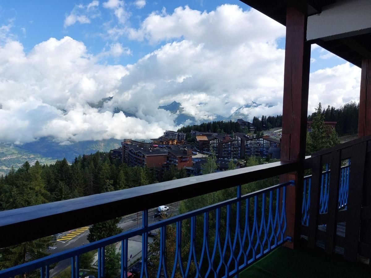 Un balcon offrant une vue sur une ville entourée de montagnes et de nuages.