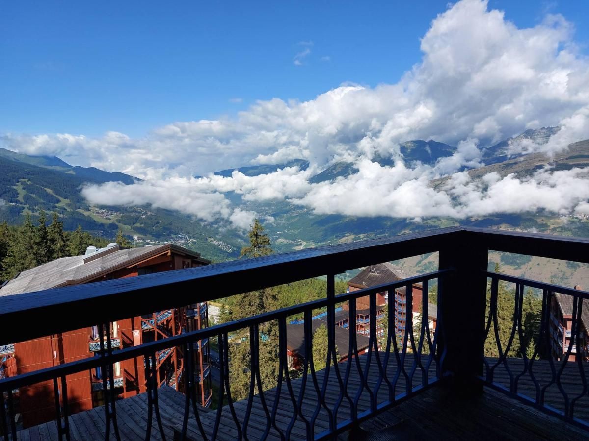 A balcony with a view of a mountainous landscape, a wooden building, and a railing.