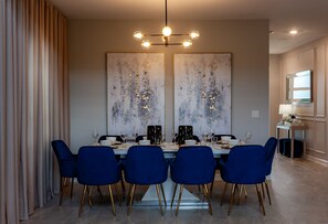 A dining area with a table set for six, blue chairs, and a modern chandelier. - 801dsd-the Retreat At Championsgate 5 Bedroom Villa by RedAwning (Kissimmee)
