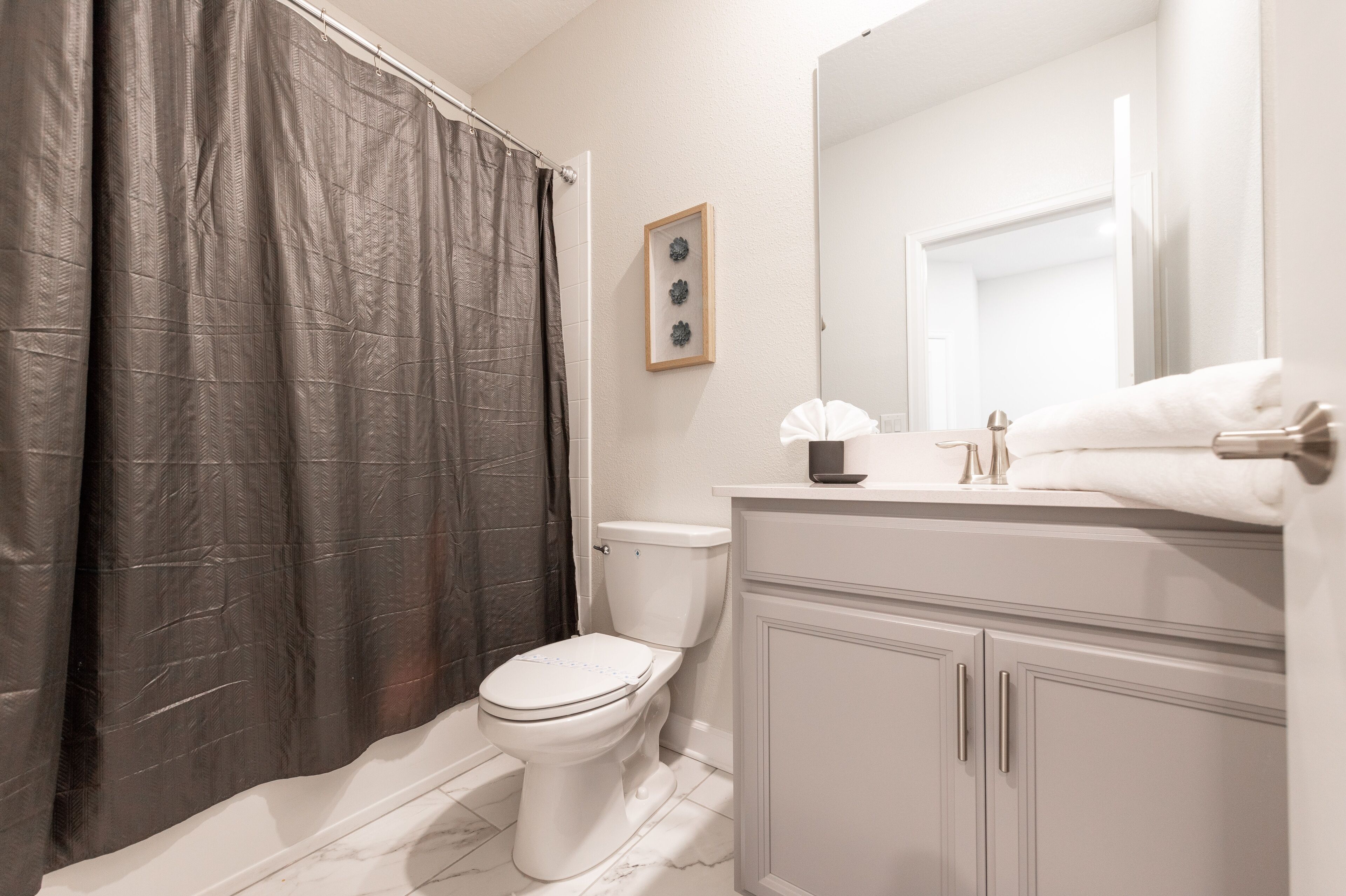 A bathroom with a toilet, a sink, a mirror, and a shower curtain.