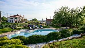 Piscina con sillas de descanso, rodeada de follaje y un muro de piedra.
