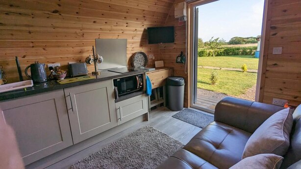 Ein gemütliches Blockhauss-Interieur mit Küchenzeile, einer Couch und einem großen Fenster mit Blick ins Freie.