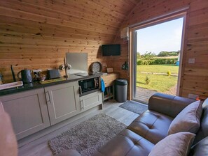 Un intérieur de chalet chaleureux avec une kitchenette, un canapé et une grande fenêtre donnant sur le paysage extérieur.