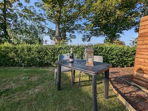 An outdoor table with a bottle and glass, surrounded by greenery and trees. - Luxury Glamping Pod With Hot Tub, Fees Apply (Mablethorpe)