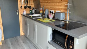 Eine kleine Küche mit Holzbalkendecke, einer eingebauten Mikrowelle, einem Toaster und einem Spülbecken mit hängendem Besteck.
