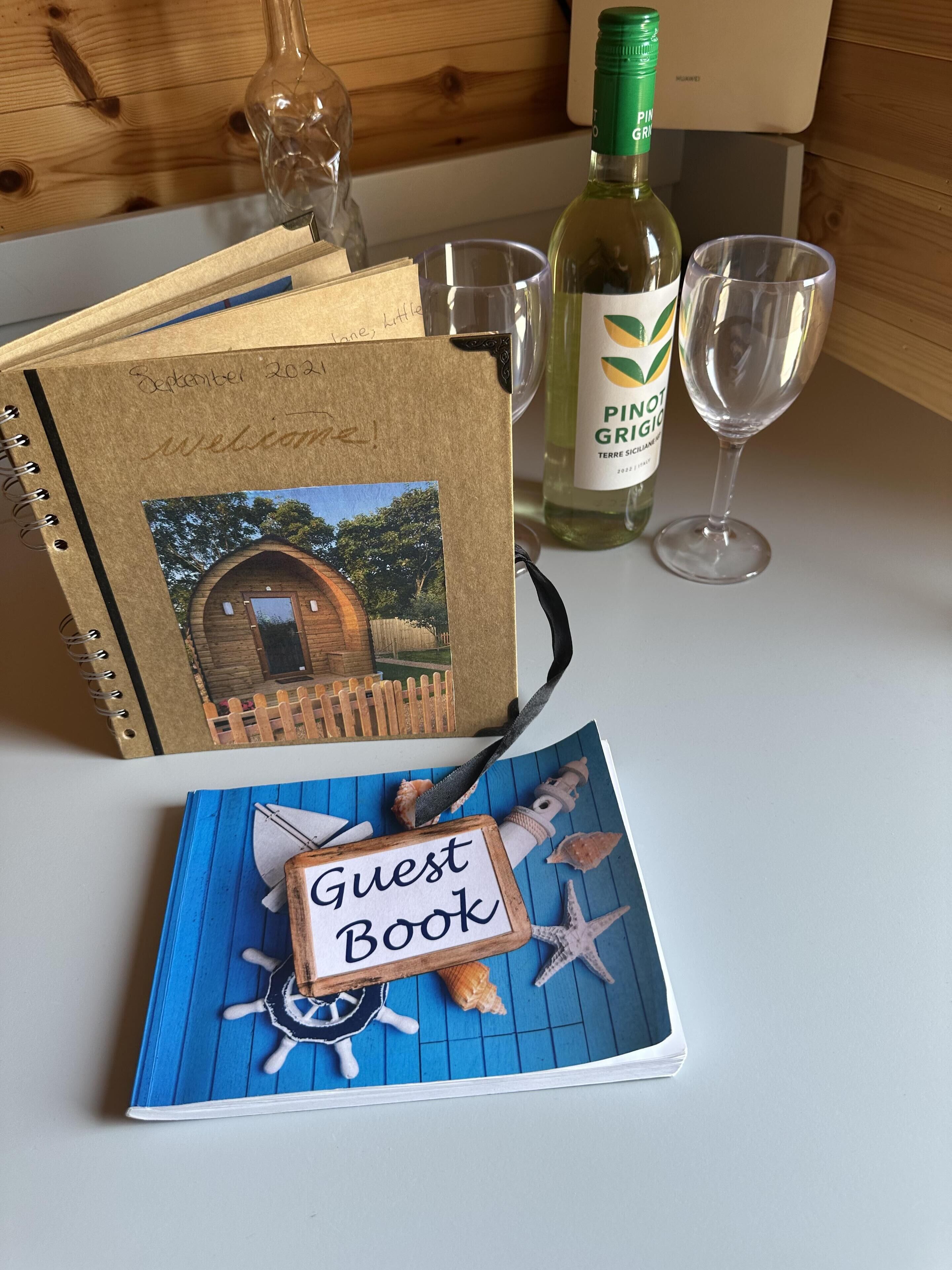 Un llibre d'aforaments amb temàtica marina, una ampolla de vi Pinot Grigio i un got sobre una taula de fusta.