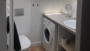 A compact, modern bathroom with a skylight, a washing machine, a toilet, and a small sink.