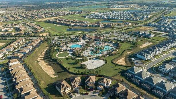 An aerial view of a residential area with houses, a golf course, and a central swimming pool. - 1233chd - The Retreat At Championsgate 9 Bedroom Home by RedAwning (Davenport)