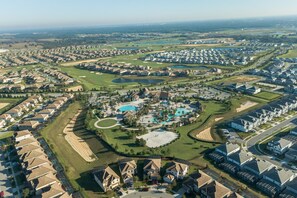 An aerial view of a residential area with houses, a golf course, and a central swimming pool. - 1233chd - The Retreat At Championsgate 9 Bedroom Home by RedAwning (Davenport)
