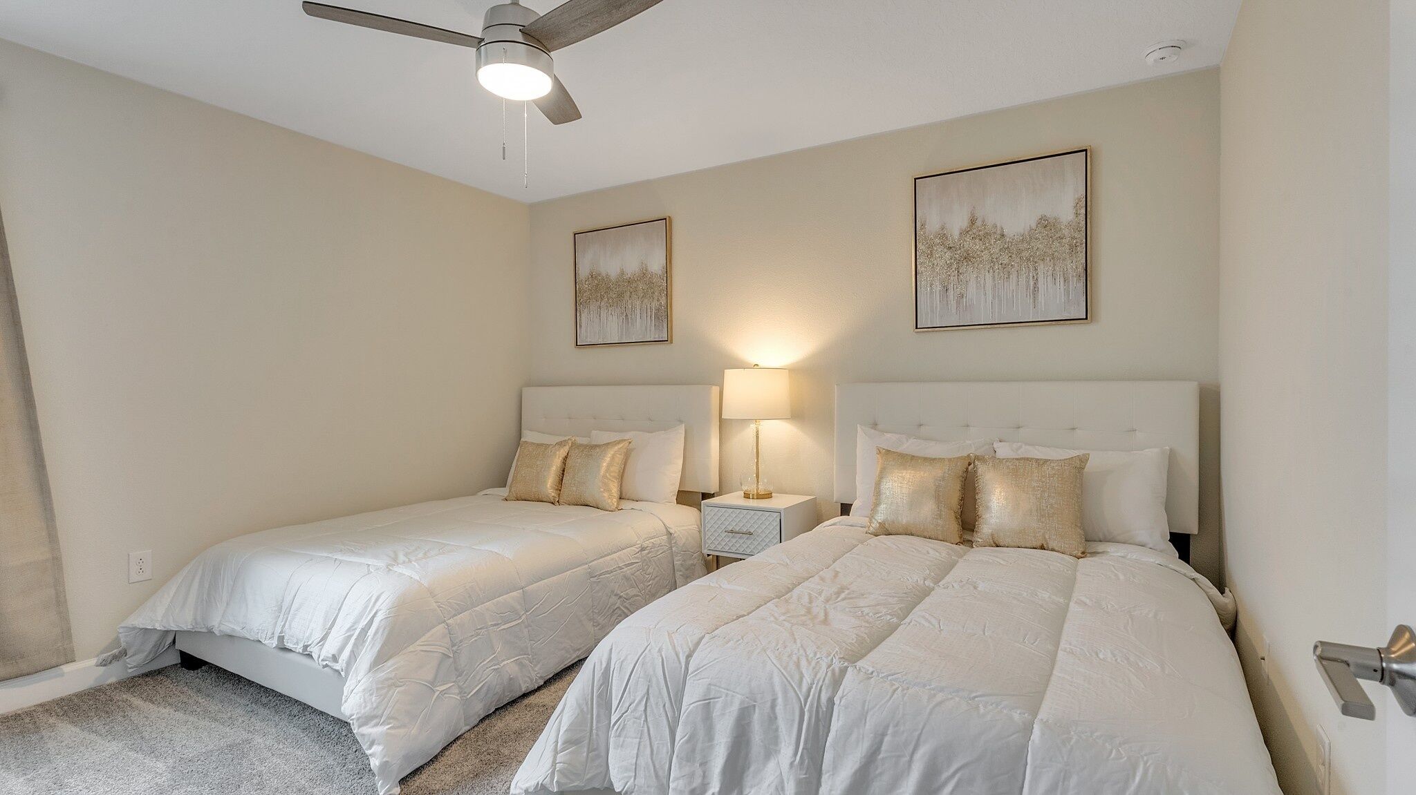A bedroom with two beds, a ceiling fan, and two wall-mounted lamps.