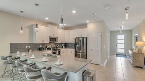 A modern kitchen with a large island, stainless steel appliances, and a bar area with stools. - 1233chd - The Retreat At Championsgate 9 Bedroom Home by RedAwning (Davenport)