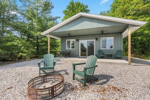 A covered outdoor seating area with Adirondack chairs and a fire pit. - Modern Comfort Secluded Getaway Fish Creek Pines (Fish Creek)