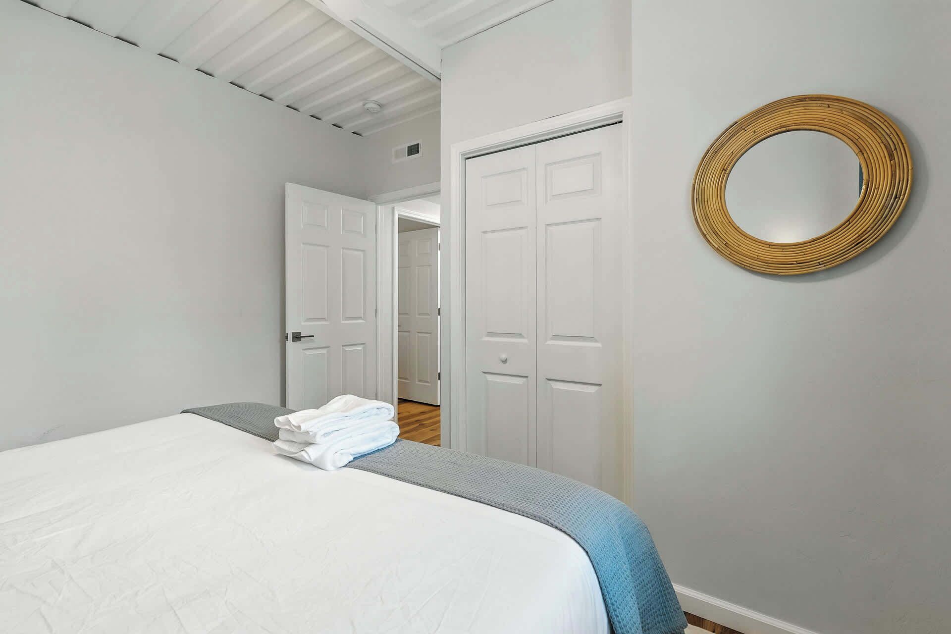 A bedroom with a bed, a door, a wall-mounted mirror, and a hallway.