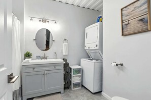 A modern bathroom with a grey vanity, a round mirror, a built-in washing machine, and a painting on the wall. - Modern Comfort Secluded Getaway Fish Creek Pines (Fish Creek)