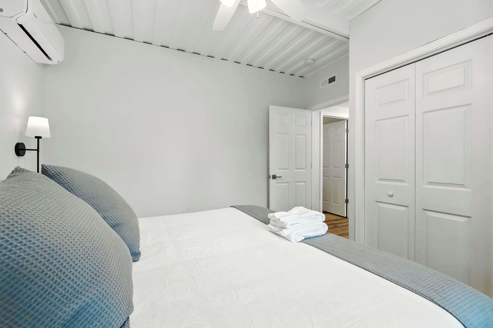 Et soveværelse med en seng, en vægmonteret lampe, en loftventilator og en dør til et andet rum.