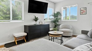 Ein modernes Wohnzimmer mit Flachbildfernseher, schwarzem Schrank, rundem Couchtisch, grauem Sessel und einer Couch.