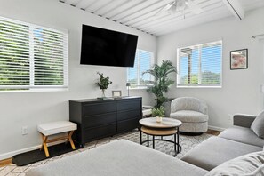 Ein modernes Wohnzimmer mit Flachbildfernseher, schwarzem Schrank, rundem Couchtisch, grauem Sessel und einer Couch.