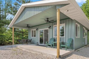 A covered outdoor area with a ceiling fan, a table with chairs, and a gravel path leading to a building with large windows and a door. - Modern Comfort Secluded Getaway Fish Creek Pines (Fish Creek)