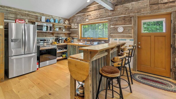 Une cuisine rustique avec des murs en bois, un réfrigérateur en acier inoxydable, un comptoir de bar en bois et une grande fenêtre.