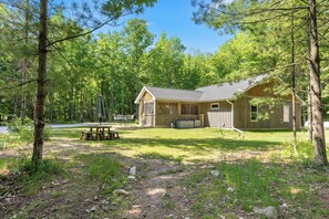 A cabin with a patio, a hot tub, and a covered outdoor seating area surrounded by trees.
