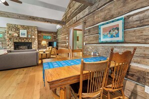 A rustic cabin interior with a stone fireplace, wooden dining table, and a cozy seating area.
