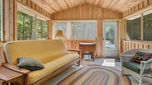 L’intérieur d’un chalet en bois, avec un canapé, un fauteuil en osier, une petite table et une grande fenêtre.