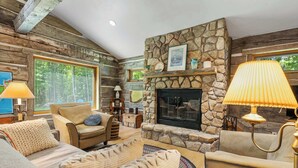 L’intérieur d’une cabane en rondins, avec une cheminée en pierre, des canapés en cuir et une grande fenêtre.