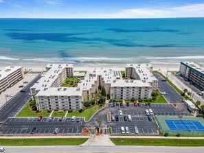 A beachfront hotel with multiple buildings, a parking lot, and a tennis court.