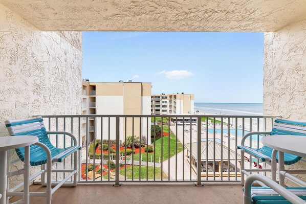 En balkon med udsigt over en strand, en pool og en anlagt have.