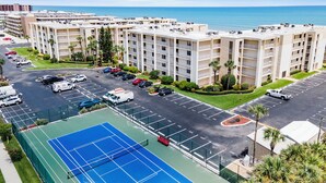 A multi-story hotel with a tennis court, parking lot, and ocean view. - 🌊Magnificent Ocean Views-Pool-Castle Reef 429🌊 (New Smyrna Beach)