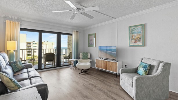 A modern living room with a sofa, armchairs, a TV, and a ceiling fan. - 🌊Magnificent Ocean Views-Pool-Castle Reef 429🌊 (New Smyrna Beach)