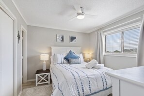 Une chambre à coucher avec un lit, des lampes de chevet, un ventilateur de plafond et une fenêtre avec des stores.