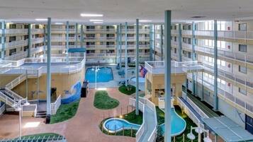 Un vestíbulo de hotel de varios niveles con una piscina central, varios balcones y una zona de juegos para niños.