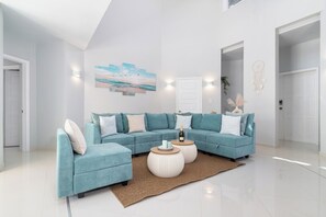 Un salon moderne avec un canapé d’angle, deux petites tables rondes et un grand tableau mural.