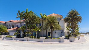 Ein mehrstöckiges Hotel mit rotem Ziegeldach, Palmen und blauem Himmel.