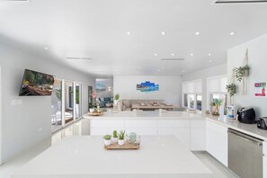 A modern kitchen with a central island, white cabinetry, and a dining area with a sofa and coffee table. - Majestic 6BR Villa w/ Private Pool near Palm Beach (Noord)
