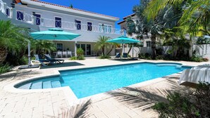 A swimming pool with lounge chairs and umbrellas, surrounded by palm trees and a building with a balcony. - Majestic 6BR Villa w Private Pool near Palm Beach (Noord)